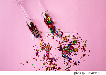 Overhead view of champagne flutes with scattered multi colored confetti on pink background Overhead view of champagne flutes with scattered multi colored confetti on pink background 85895859