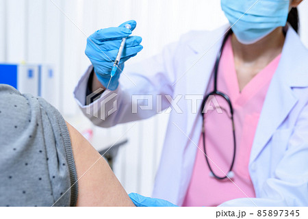 診察室で女性高齢者にワクチン接種の注射をするスクラブを着てマスクをした女性医療従事者　外来　診察 85897345