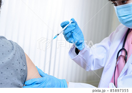 診察室で女性高齢者にワクチン接種の注射をするスクラブを着てマスクをした女性医療従事者　外来　診察 85897355