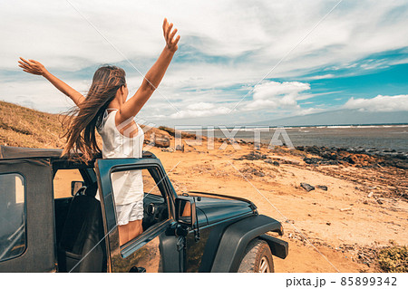 Car road trip travel fun happy woman tourist with open arms at ocean view from sports utility car driving on beach. Summer vacation adventure girl from the back 85899342