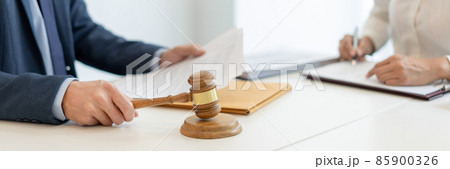 law concept the legal representative in deep blue suit gavel to approve agreement in the official document that the company submits to him while his aider sitting at the same desk with him 85900326