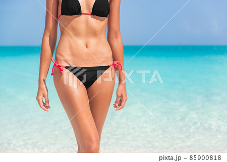 Bikini body woman on summer ocean beach vacation travel background. Tanned skin for sun skincare, laser therapy hair removal sexy legs concept. Closeup of slim stomach and hips Bikini body woman on summer ocean beach vacation travel background. Tanned skin for sun skincare, laser therapy hair removal sexy legs concept. Closeup of slim stomach and hips 85900818