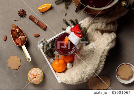 A glass of mulled wine decorated with a cinnamon stick and a New Year's cap, a knitted plaid, tangerines and fir branches. Flatlay 85901064