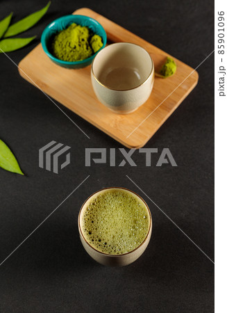 Japanese matcha tea in a bowl, close-up on a black background. Leaves, a bowl with tea powder in the background. Vertical 85901096