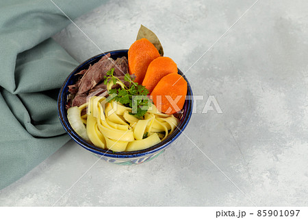 Lagman, homemade pulled noodles, vegetables and boiled meat. In a painted bowl, close-up on a gray background. Copy of the space 85901097