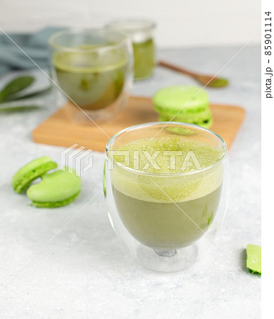 Matcha green tea with foam in glass glasses and green macaroon cakes. Close-up, on a gray background, selective focus Matcha green tea with foam in glass glasses and green macaroon cakes. Close-up, on a gray background, selective focus 85901114
