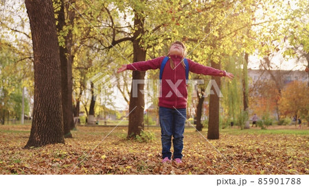 little girl with backpack throws autumn leaves up and laughs, cheerful child plays with leaf fall city street, joyful kid having fun park after school lessons, happy family, children's fantasy dreams 85901788