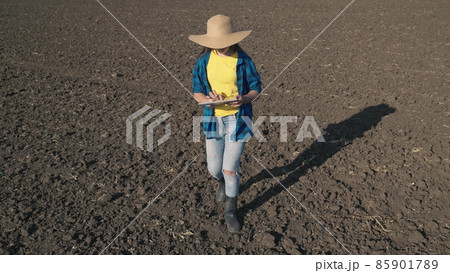 a farmer with a tablet walks on a plowed field of land with a tablet, work on a plantation, farming farming, an agronomist prepares to plant seedlings in organic soil of the land, business production 85901789