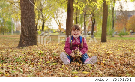 happy girl throws autumn yellow leaves up and laughs, kid is having fun playing in city nature park outdoors, little child with school backpack sits under leaf fall, first grader school yard having happy girl throws autumn yellow leaves up and laughs, kid is having fun playing in city nature park outdoors, little child with school backpack sits under leaf fall, first grader school yard having 85901851