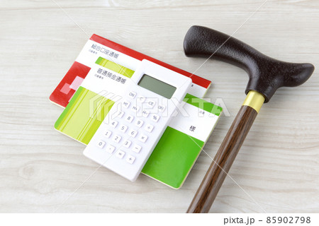老後・介護の金銭的な備えイメージ―レプリカの通帳と高齢者用の杖と電卓 85902798