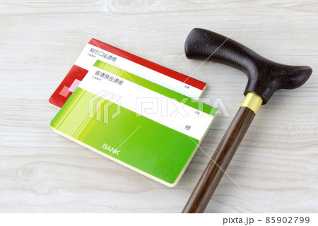 老後・介護の金銭的な備えイメージ―レプリカの通帳と高齢者用の杖 85902799