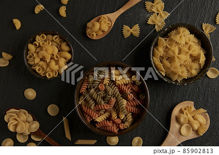 pasta concept some of various kinds of pasta put into a small bowl, some put on a wooden spoon, and some put on the dark background 85902813