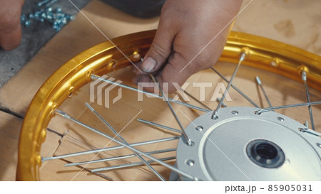 Technician man working motorcycle wheel has spokes weave up on mechanic new steel wheel Technician man working motorcycle wheel has spokes weave up on mechanic new steel wheel 85905031
