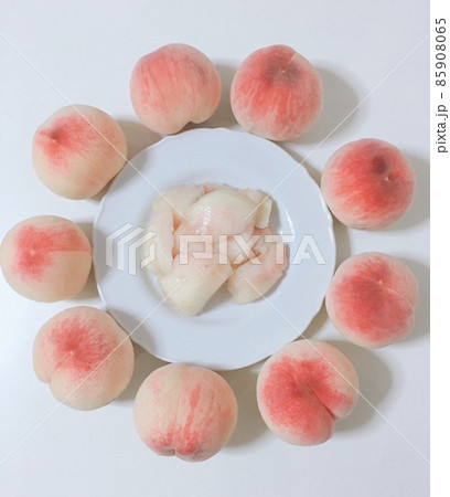 白い皿の周りに円を描くたくさんの採れたてのピンクの桃とカットされたみずみずしい桃 白い皿の周りに円を描くたくさんの採れたてのピンクの桃とカットされたみずみずしい桃 85908065