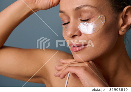 Head shot of a young beautiful woman with perfect glowing skin and natural makeup posing for the camera with medical collagen patches under her eyes to reduce fatigue and puffiness. Skin care concept 85908610