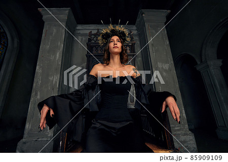 Portrait of a beautiful medieval young woman in black dress In stylish crown sitting on a throne. The Middle Ages history 85909109