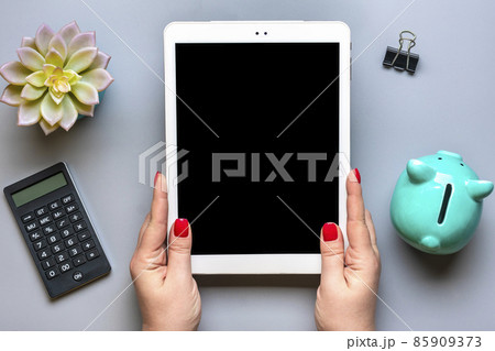 female hands holds digital tablet with black screen, piggy bank, calculator, succulent, notebook on gray background Business, insurance, technology concept Top view Flat lay Mock up Home workplace female hands holds digital tablet with black screen, piggy bank, calculator, succulent, notebook on gray background Business, insurance, technology concept Top view Flat lay Mock up Home workplace 85909373