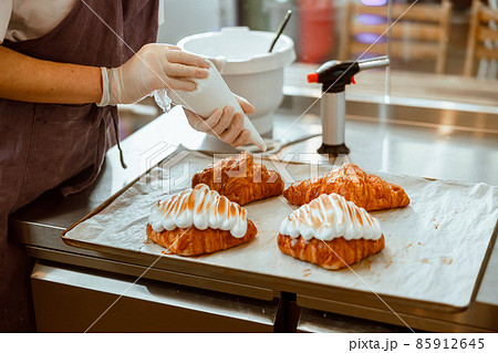 Worker in brownapron applies albumenous cream onto croissant in craft bakery shop 85912645