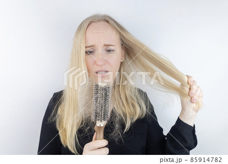 Close-up of a girl whose hair is falling out. There is a large tuft of tangled curls on the comb. The blonde looks upset into the frame. The concept of women problems with the scalp 85914782