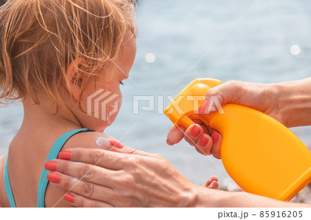 Mother applying sunscreen to her child at a beach 85916205