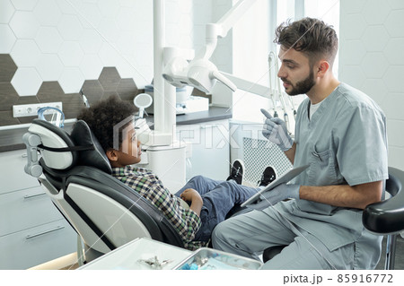 Young confident dentist with tablet consulting little patient 85916772
