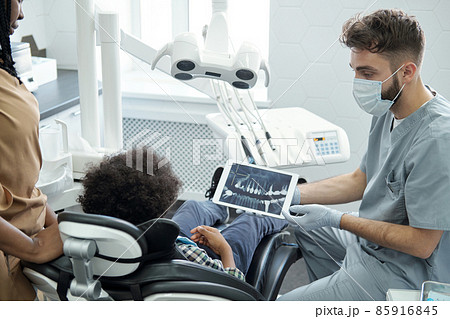 Dentist in protective workwear showing jaw x-ray to little patient 85916845