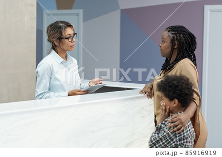 African woman with son consulting with receptionist by counter 85916919
