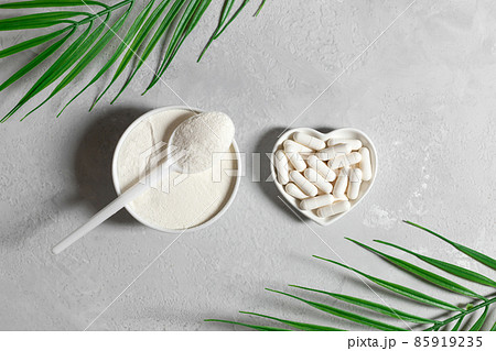 Collagen on a gray background with palm leaves. Collagen powder and pills. Fish or plant based supplement. Top view, flat lay. 85919235