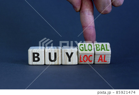 Buy local or global symbol. Businessman turns wooden cubes, changes words 'buy local' to 'buy global'. Beautiful grey table, grey background. Business, buy local or global concept. Copy space. Buy local or global symbol. Businessman turns wooden cubes, changes words 'buy local' to 'buy global'. Beautiful grey table, grey background. Business, buy local or global concept. Copy space. 85921474