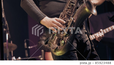 Man saxophonist at a concert plays the saxophone. Live musical performance and virtuosity of playing a brass musical instrument. It dark, colored spotlights are shining around 85923488
