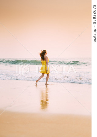Goa, India. Young Caucasian Woman In Yellow Dress Enjoying Life And Running Towards Sea Waves 85923678