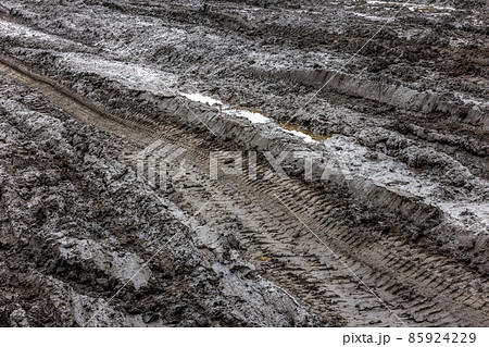 A broken rural country road after the rain. Puddles after rain on a dirt road. Clay, soil and puddles at cloudy day light after rain, autumn season. 85924229