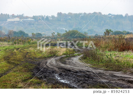 autumnal foggy morning rustic lansdcape with dirt road in the foreground and small buildings on hill in the background autumnal foggy morning rustic lansdcape with dirt road in the foreground and small buildings on hill in the background 85924253