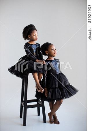 Adorable african sisters in black dresses posing in studio Adorable african sisters in black dresses posing in studio 85924938