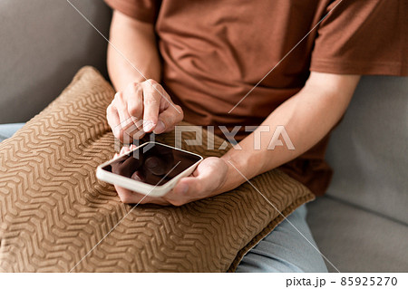 Technology Concept The man sitting next to a pot of plant, putting a small pillow on his lap, and checking something on his smartphone Technology Concept The man sitting next to a pot of plant, putting a small pillow on his lap, and checking something on his smartphone 85925270
