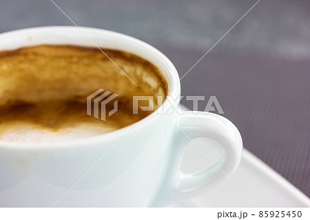 Round white ceramic cup with cappuccino latte coffee brown foam on square saucer on a table. A hot flavored aromatic drink in a cafe, restaurant in the morning, lunch time. Beverage theme, copy space. Round white ceramic cup with cappuccino latte coffee brown foam on square saucer on a table. A hot flavored aromatic drink in a cafe, restaurant in the morning, lunch time. Beverage theme, copy space. 85925450