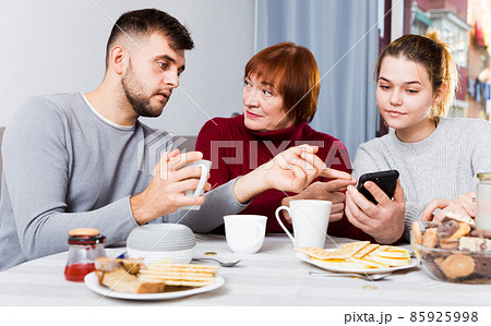 Senior woman with adult children using mobile gadget Senior woman with adult children using mobile gadget 85925998