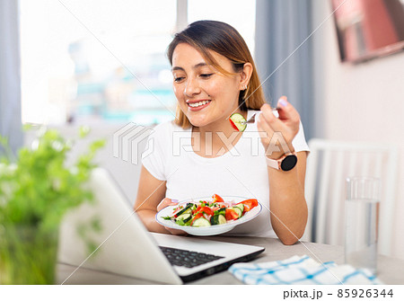 Housewife watching movie on laptop and eating vegetable salad 85926344