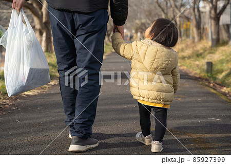 買い物袋を持ち子供と歩く男性の後ろ姿 85927399