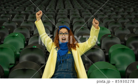 Caucasian woman cheers for a sports team at the stadium. The girl watches the match at the stadium alone. Caucasian woman cheers for a sports team at the stadium. The girl watches the match at the stadium alone. 85930278