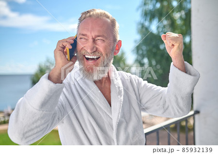 High-spirited man standing on the balcony during the phone conversation 85932139