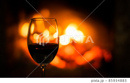 A wineglass of red wine on the background of the fireplace lights. Christmas holiday concept 85934883