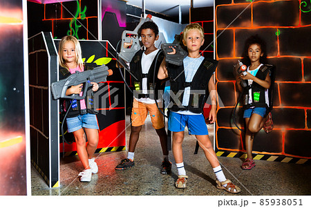 Joyful teens aiming laser guns at other players during lasertag game in dark room 85938051