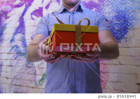Man in blue shirt holds out a box with a gift indoors Man in blue shirt holds out a box with a gift indoors 85938945