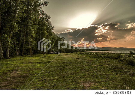 The evening sky with a red sunset from huge clouds, over a forest belt with a clearing next to the shore of Lake Sevan in Armenia. The evening sky with a red sunset from huge clouds, over a forest belt with a clearing next to the shore of Lake Sevan in Armenia. 85939303