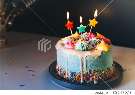 Colorful birthday cake with sprinkles and burning star shaped candles on a dark wall background. Festive birthday celebration, party. Selective focus, copy space Colorful birthday cake with sprinkles and burning star shaped candles on a dark wall background. Festive birthday celebration, party. Selective focus, copy space 85947078