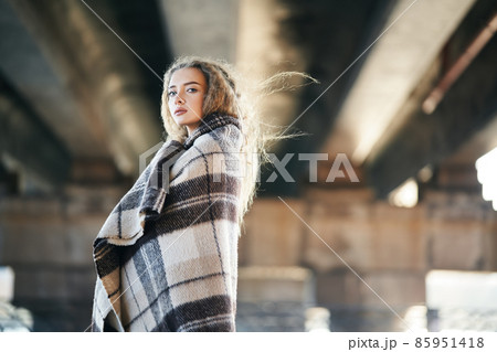 Portrait of pretty confident woman wrapped in wool blanket looking to camera posing on urban street background with copy space 85951418