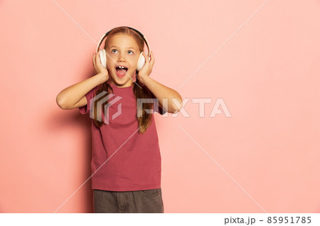 Happy little girl wearing t-shirt listening to music in headphones isolated on pink background. Concept of childhood, emotions, study 85951785