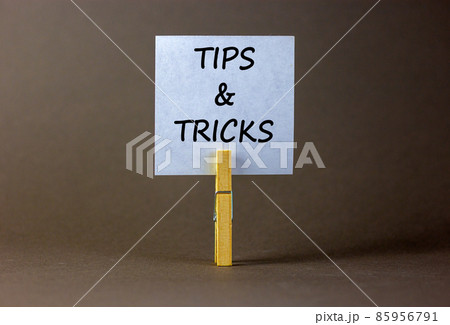 Tips and tricks symbol. White paper on wooden clothespin. Words 'Tips and tricks'. Beautiful grey background. Business and tips and tricks concept, copy space. 85956791