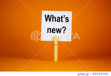 White paper with text 'Whats New', clip on wood clothespin. Beautiful orange background. Business concept. Copy space. White paper with text 'Whats New', clip on wood clothespin. Beautiful orange background. Business concept. Copy space. 85956792